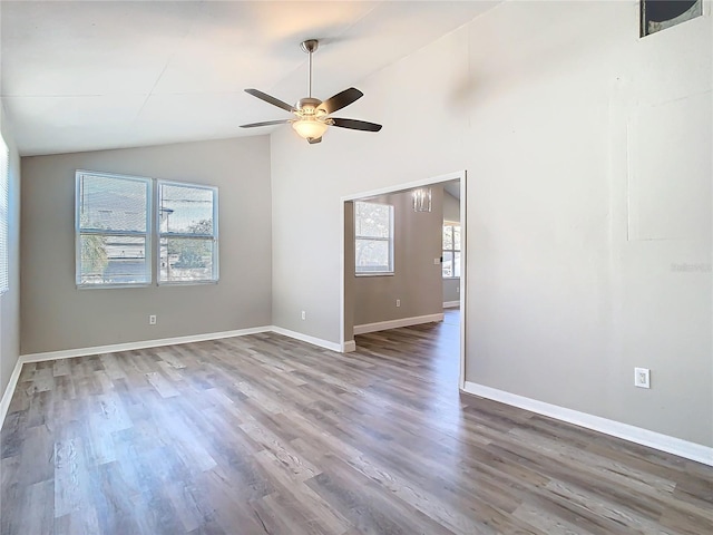 spare room with lofted ceiling, wood finished floors, a wealth of natural light, and baseboards