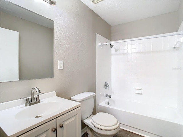 bathroom featuring toilet, a textured wall, washtub / shower combination, and vanity