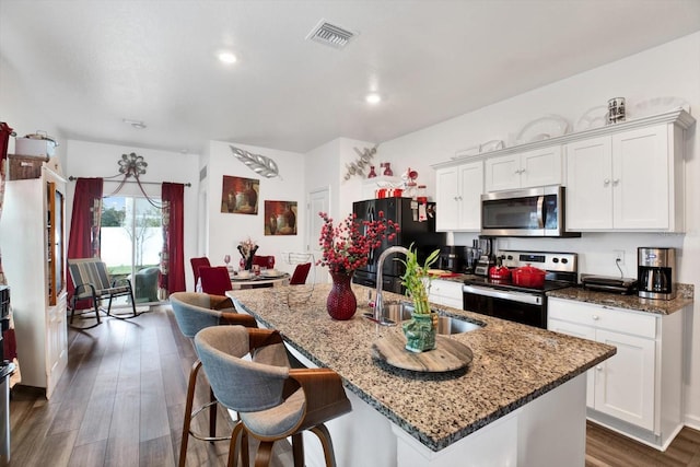 kitchen with a kitchen island with sink, stainless steel appliances, a sink, white cabinets, and dark stone counters