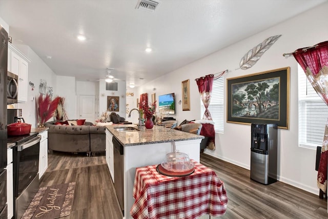 kitchen with stainless steel appliances, open floor plan, a kitchen island with sink, a sink, and white cabinets