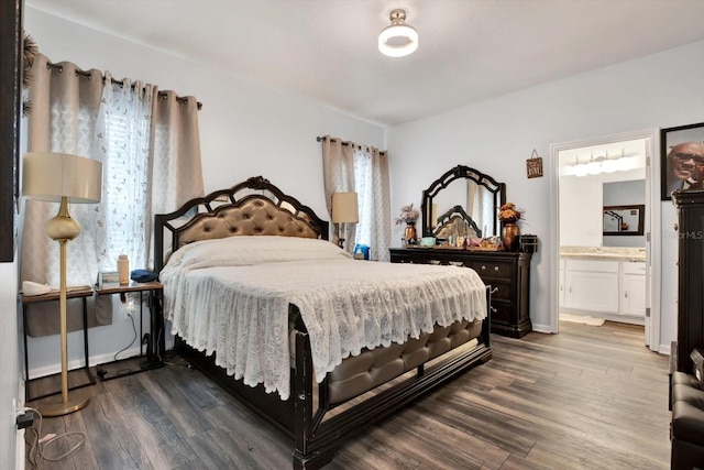 bedroom with dark wood finished floors, ensuite bath, and baseboards