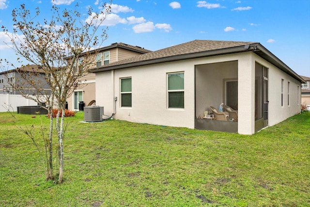 back of property featuring central AC unit, a shingled roof, a sunroom, a yard, and stucco siding