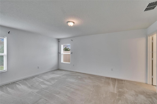 empty room with baseboards, visible vents, a textured ceiling, and light colored carpet