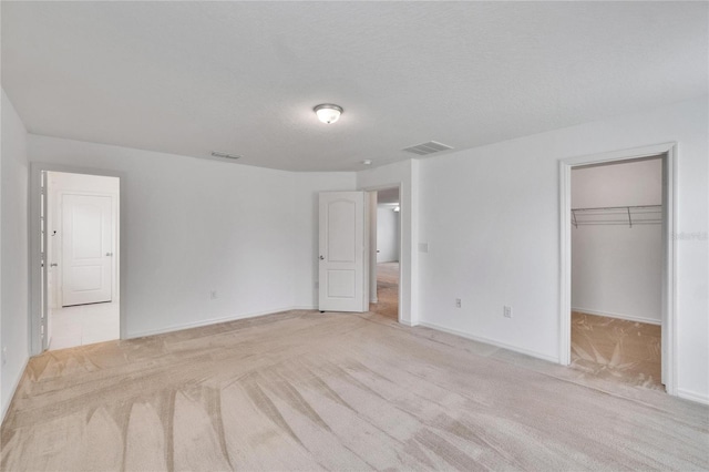 unfurnished bedroom featuring baseboards, a spacious closet, visible vents, and light colored carpet