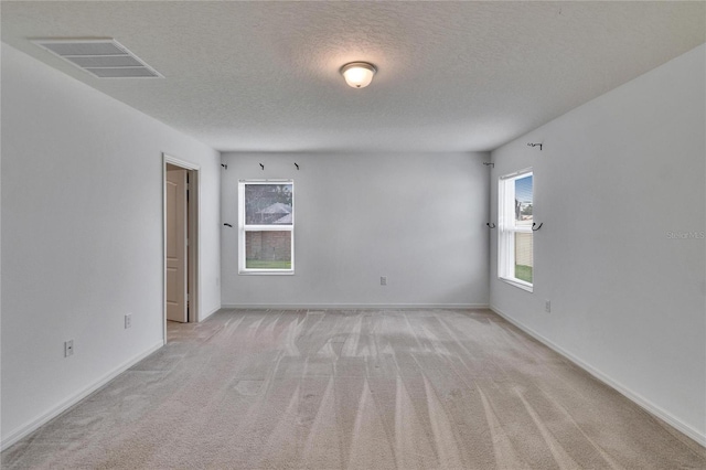 unfurnished room with baseboards, visible vents, a textured ceiling, and light colored carpet