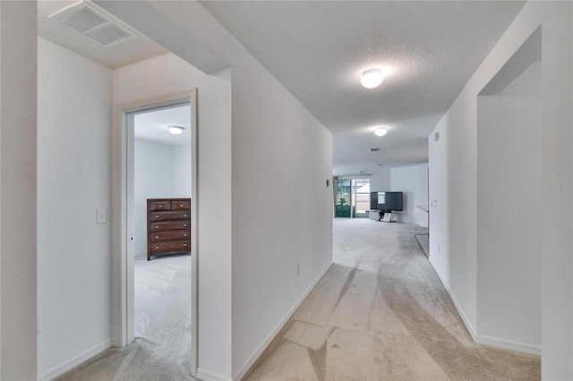 corridor with a textured ceiling, baseboards, visible vents, and light colored carpet