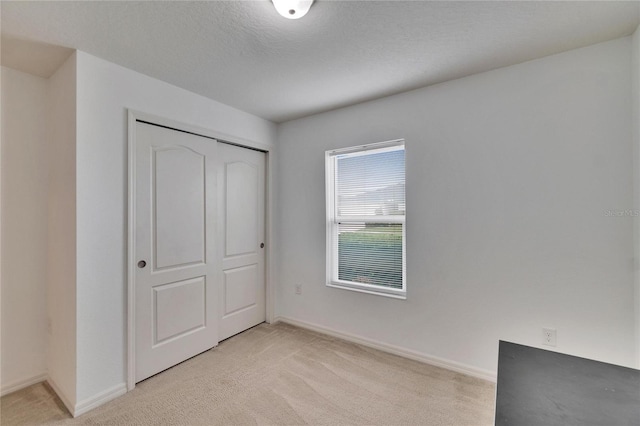 unfurnished bedroom with a closet, light carpet, and baseboards