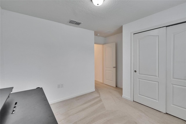 unfurnished bedroom with a closet, light colored carpet, visible vents, a textured ceiling, and baseboards