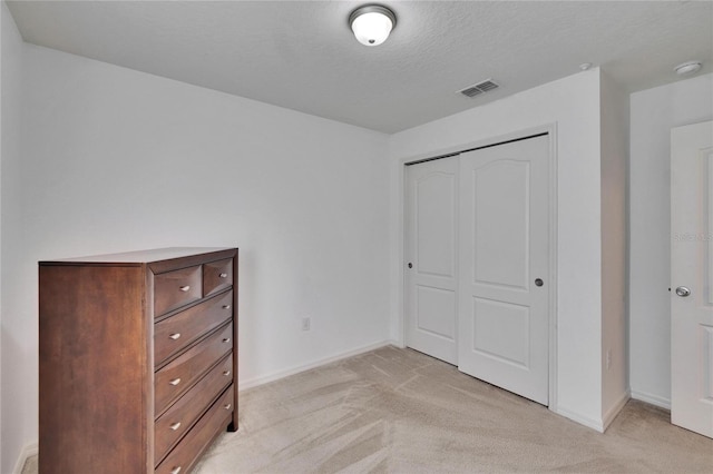 unfurnished bedroom with baseboards, visible vents, light colored carpet, a textured ceiling, and a closet