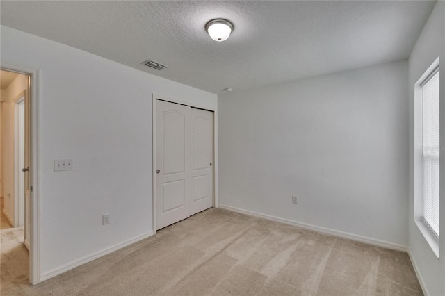 unfurnished bedroom featuring baseboards, visible vents, light colored carpet, a textured ceiling, and a closet