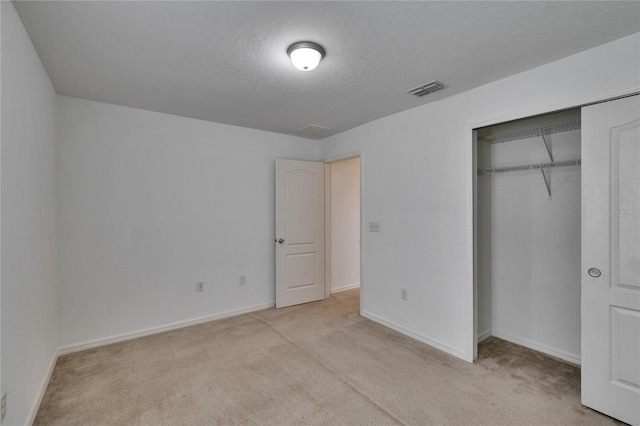 unfurnished bedroom featuring a textured ceiling, light colored carpet, visible vents, baseboards, and a closet