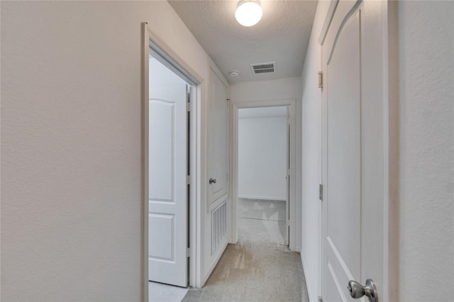 hallway featuring light colored carpet, a textured wall, visible vents, and a textured ceiling