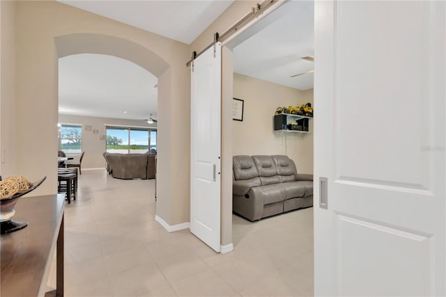 corridor featuring arched walkways, a barn door, light tile patterned flooring, and baseboards