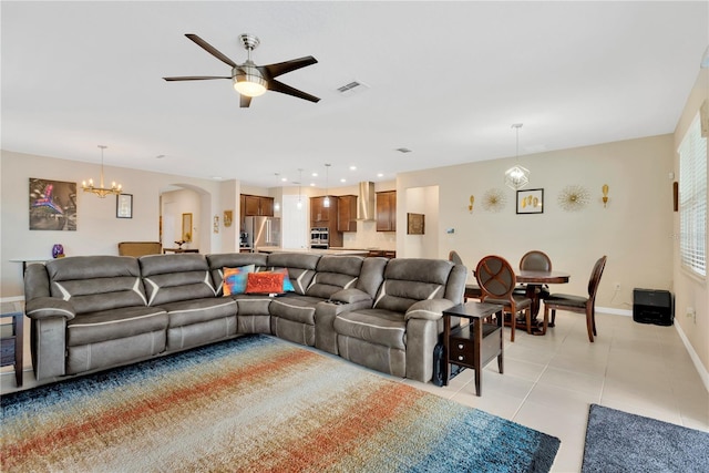 living room featuring light tile patterned floors, baseboards, visible vents, arched walkways, and ceiling fan with notable chandelier