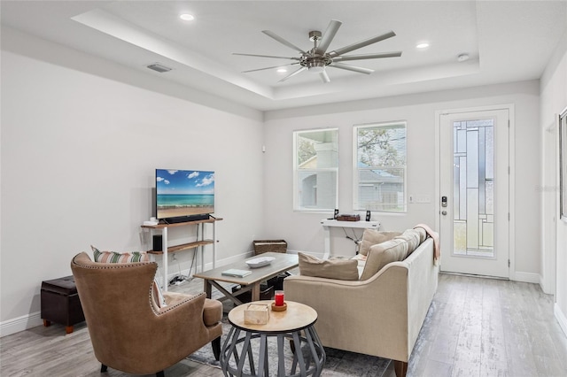 living area featuring light wood-type flooring, a raised ceiling, visible vents, and baseboards