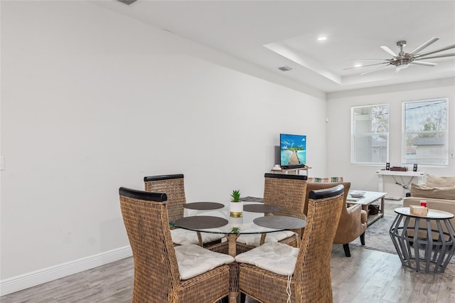 dining area featuring light wood finished floors, baseboards, a tray ceiling, and ceiling fan