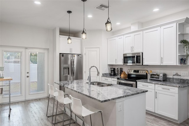 kitchen with a center island with sink, appliances with stainless steel finishes, white cabinetry, open shelves, and a sink