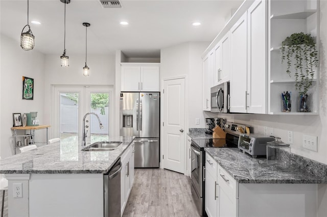 kitchen featuring pendant lighting, stainless steel appliances, a kitchen island with sink, white cabinetry, and a sink