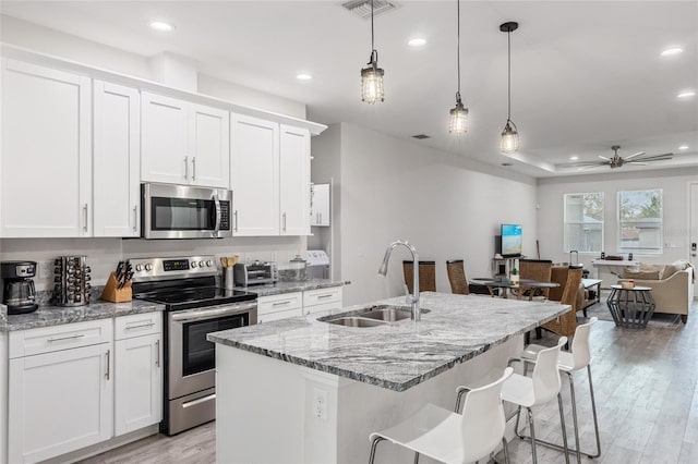 kitchen with appliances with stainless steel finishes, open floor plan, a kitchen island with sink, white cabinetry, and a sink