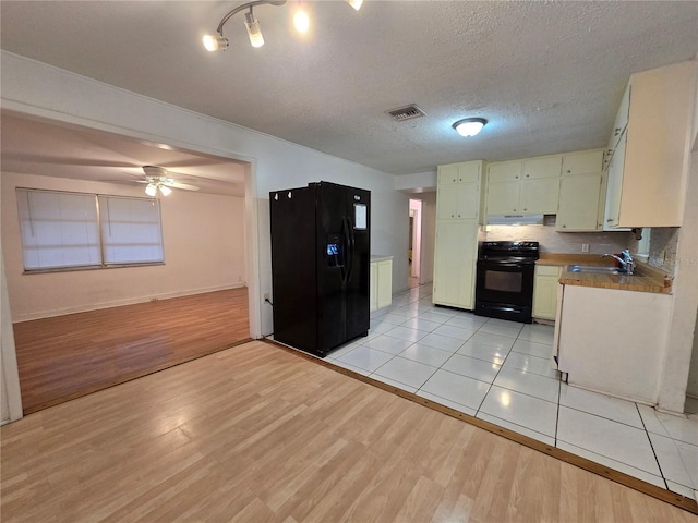 kitchen featuring a textured ceiling, visible vents, backsplash, black appliances, and light wood finished floors