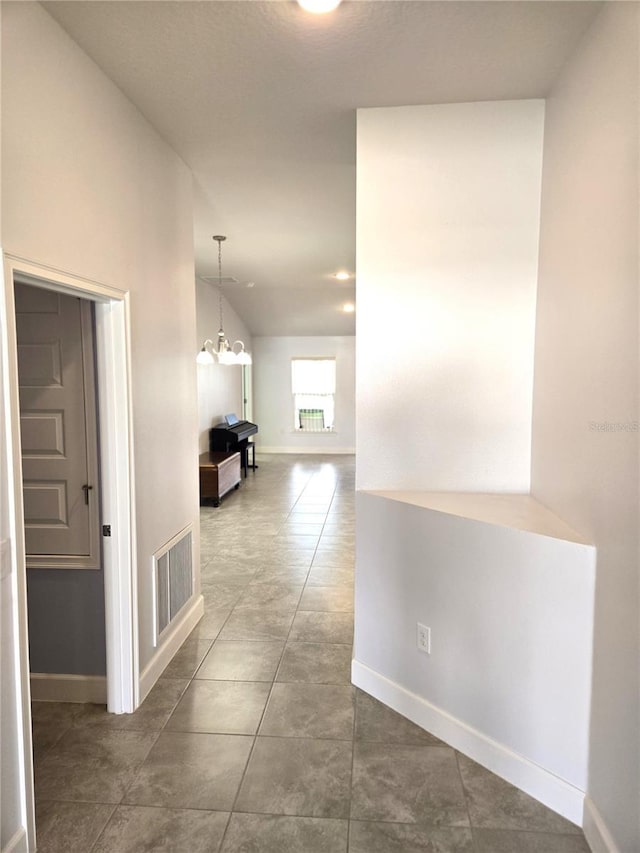 hallway with baseboards, visible vents, tile patterned floors, an inviting chandelier, and vaulted ceiling