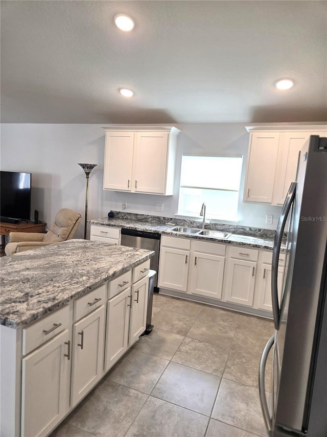 kitchen featuring a center island, light stone countertops, stainless steel appliances, white cabinetry, and a sink