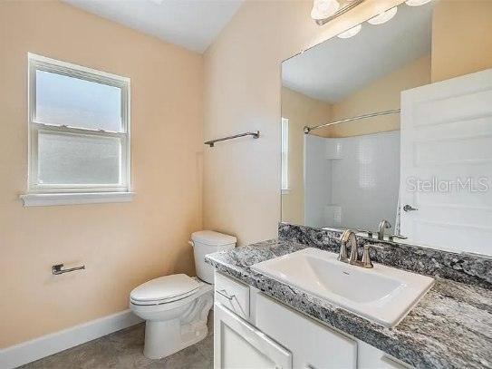 bathroom with toilet, baseboards, a shower, and vanity