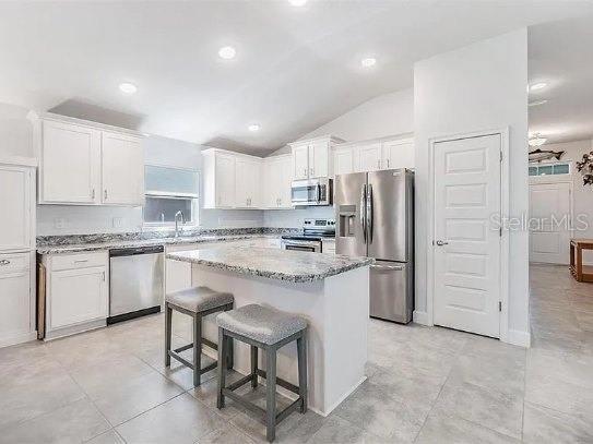 kitchen with a center island, stainless steel appliances, white cabinets, a sink, and light stone countertops