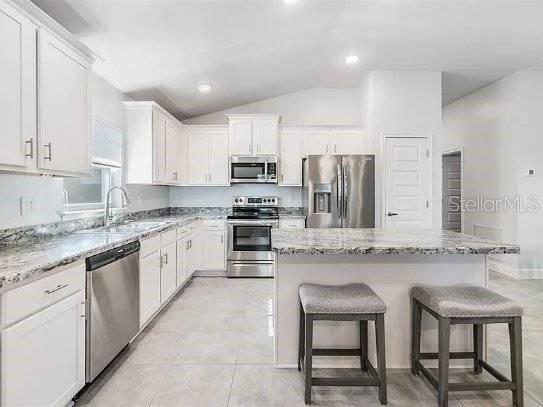 kitchen featuring a kitchen bar, white cabinetry, stainless steel appliances, and a sink