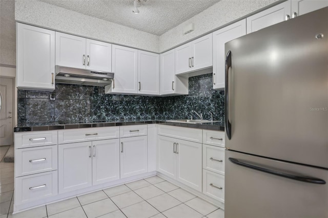 kitchen featuring dark countertops, under cabinet range hood, white cabinetry, and freestanding refrigerator