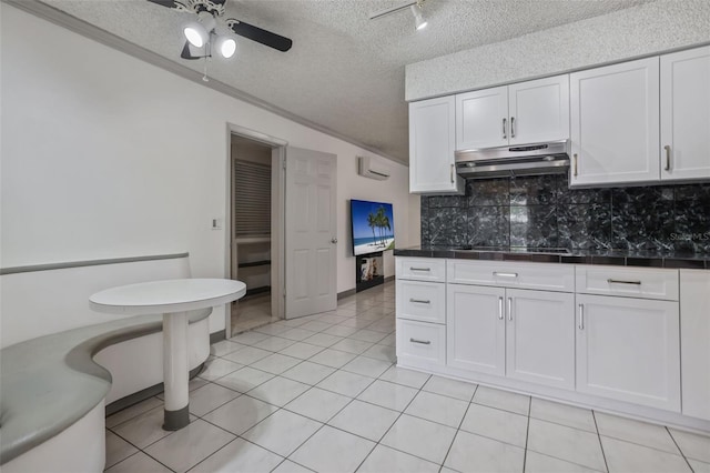 kitchen with a textured ceiling, black electric stovetop, under cabinet range hood, white cabinetry, and backsplash