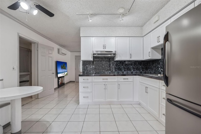 kitchen with dark countertops, under cabinet range hood, white cabinetry, and freestanding refrigerator