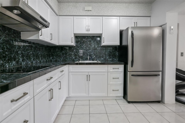 kitchen with black electric stovetop, dark countertops, freestanding refrigerator, white cabinetry, and ventilation hood