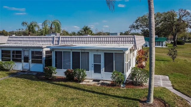 rear view of property with a sunroom, a tile roof, and a lawn