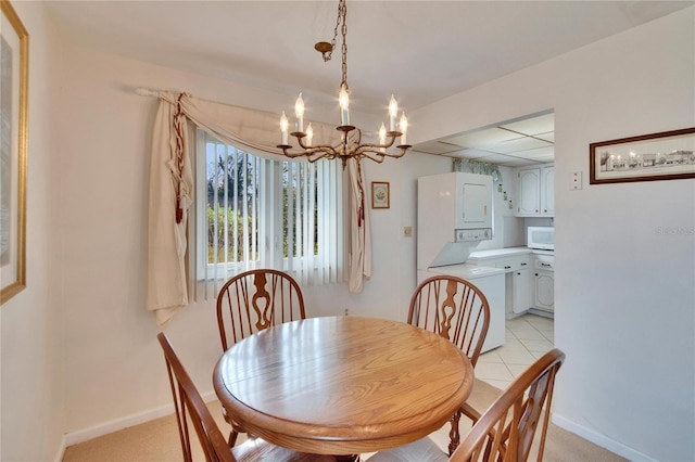 dining space with a chandelier, stacked washer / dryer, a drop ceiling, and baseboards