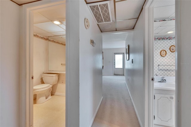 hallway featuring carpet flooring, a sink, a drop ceiling, and baseboards