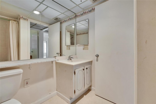 bathroom with baseboards, visible vents, a drop ceiling, toilet, and vanity