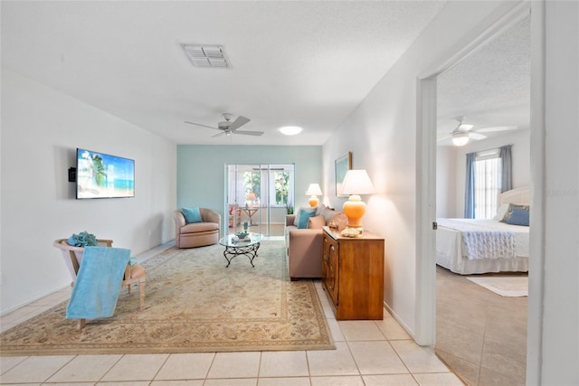 living room featuring light tile patterned floors, a textured ceiling, visible vents, and a ceiling fan