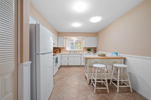 kitchen with light tile patterned flooring, white appliances, a sink, light countertops, and wainscoting