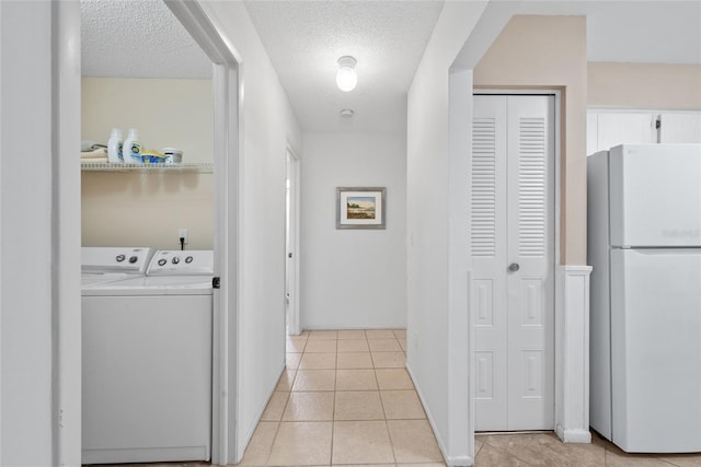 hall featuring independent washer and dryer, a textured ceiling, and light tile patterned floors