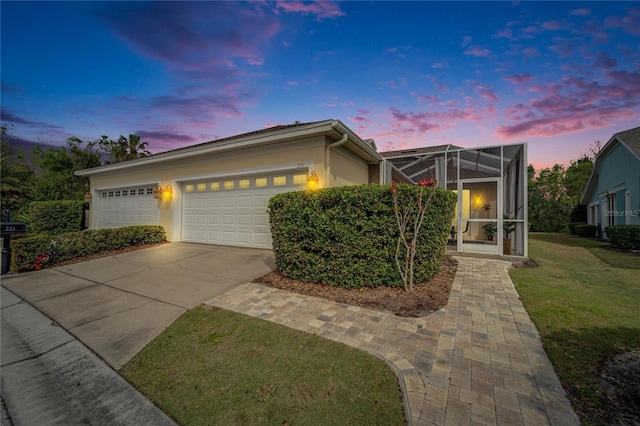 view of front of home with concrete driveway, glass enclosure, stucco siding, an attached garage, and a front yard