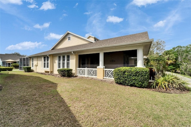 rear view of house featuring a shingled roof, a lawn, and stucco siding