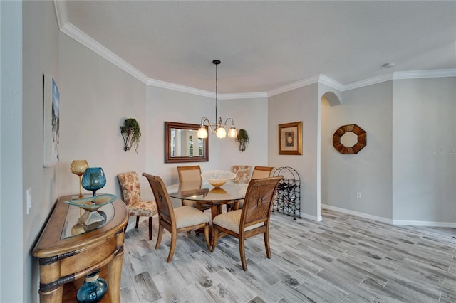 dining space featuring arched walkways, a chandelier, baseboards, light wood-style floors, and crown molding