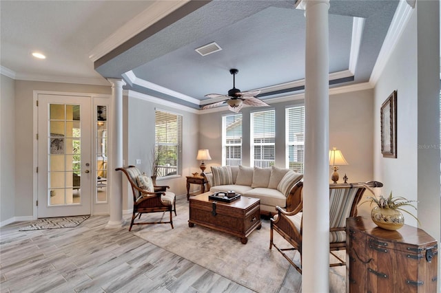 living room with a tray ceiling, visible vents, ceiling fan, light wood-type flooring, and ornate columns