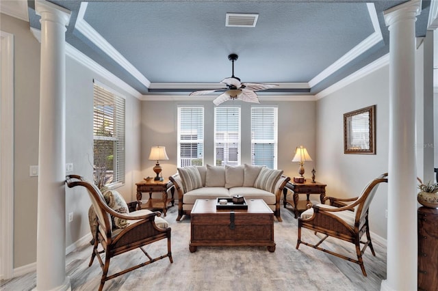 living area with decorative columns, visible vents, ceiling fan, a tray ceiling, and light wood-type flooring