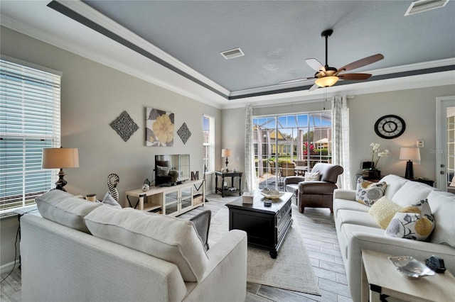 living room with visible vents, a raised ceiling, and ornamental molding