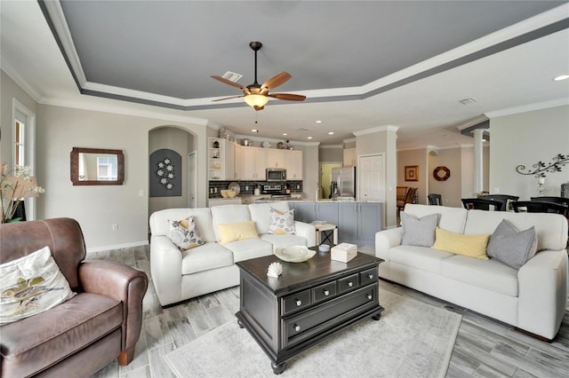 living area featuring crown molding, a tray ceiling, decorative columns, and arched walkways