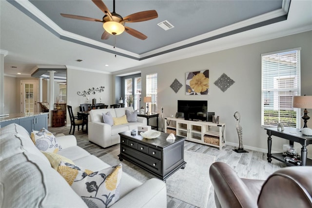 living area with a tray ceiling, a healthy amount of sunlight, visible vents, and decorative columns