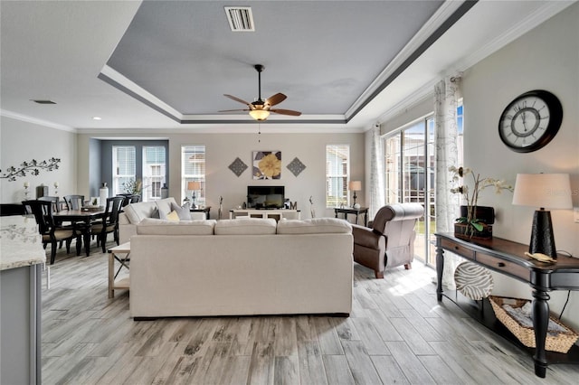 living area featuring ornamental molding, light wood-type flooring, a raised ceiling, and visible vents