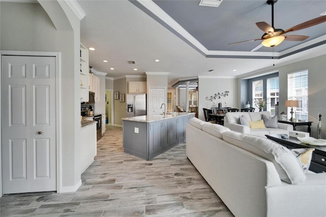 kitchen with a tray ceiling, a center island with sink, stainless steel appliances, open floor plan, and white cabinetry